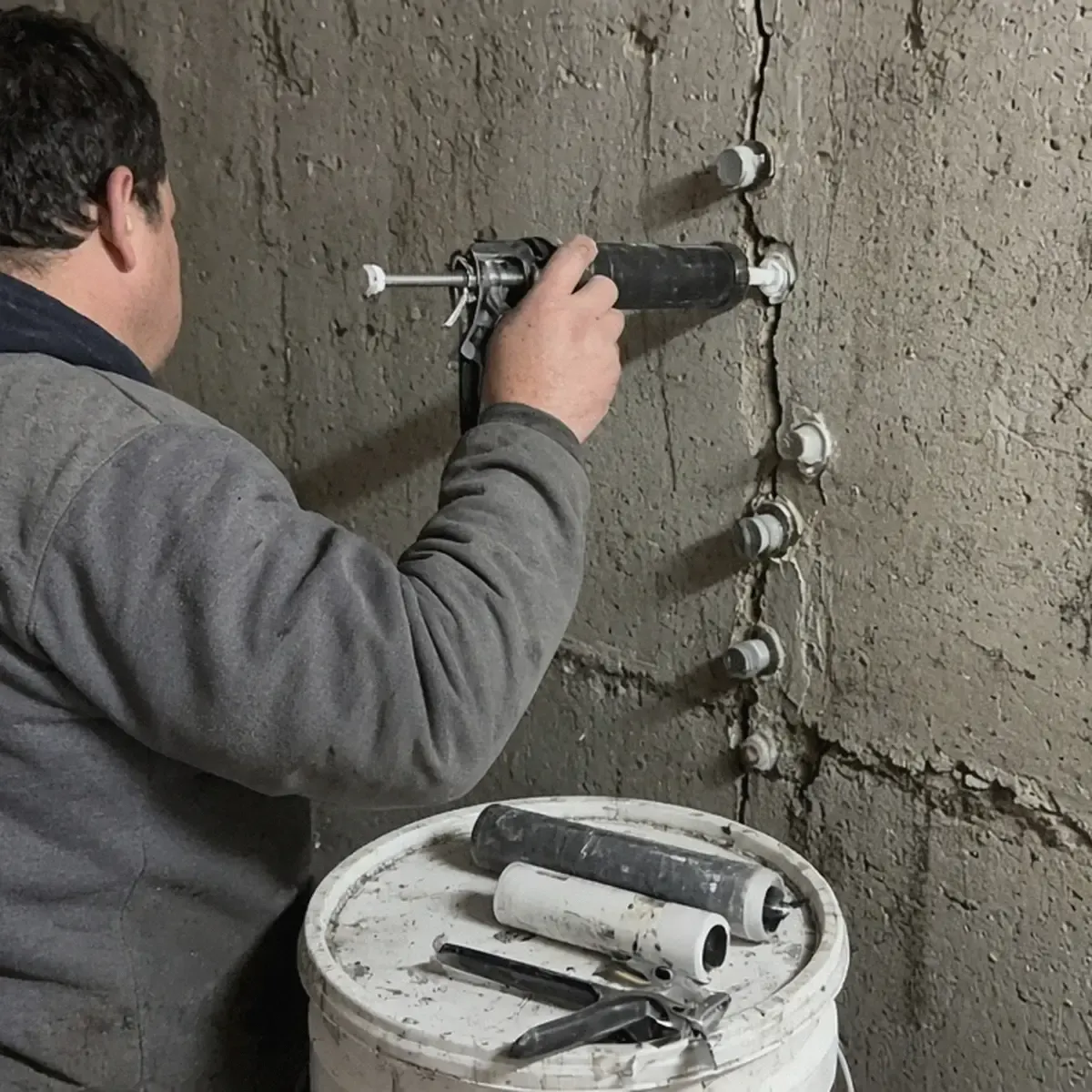 Person injecting epoxy into ports along a basement wall crack