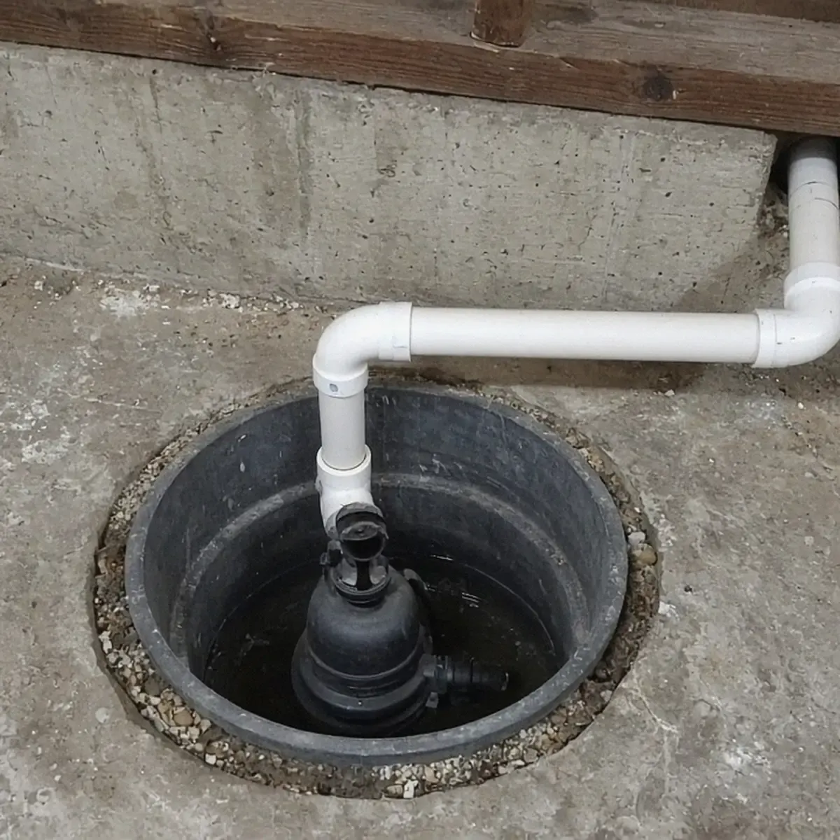Sump pit with a pump and a PVC discharge pipe in a basement floor